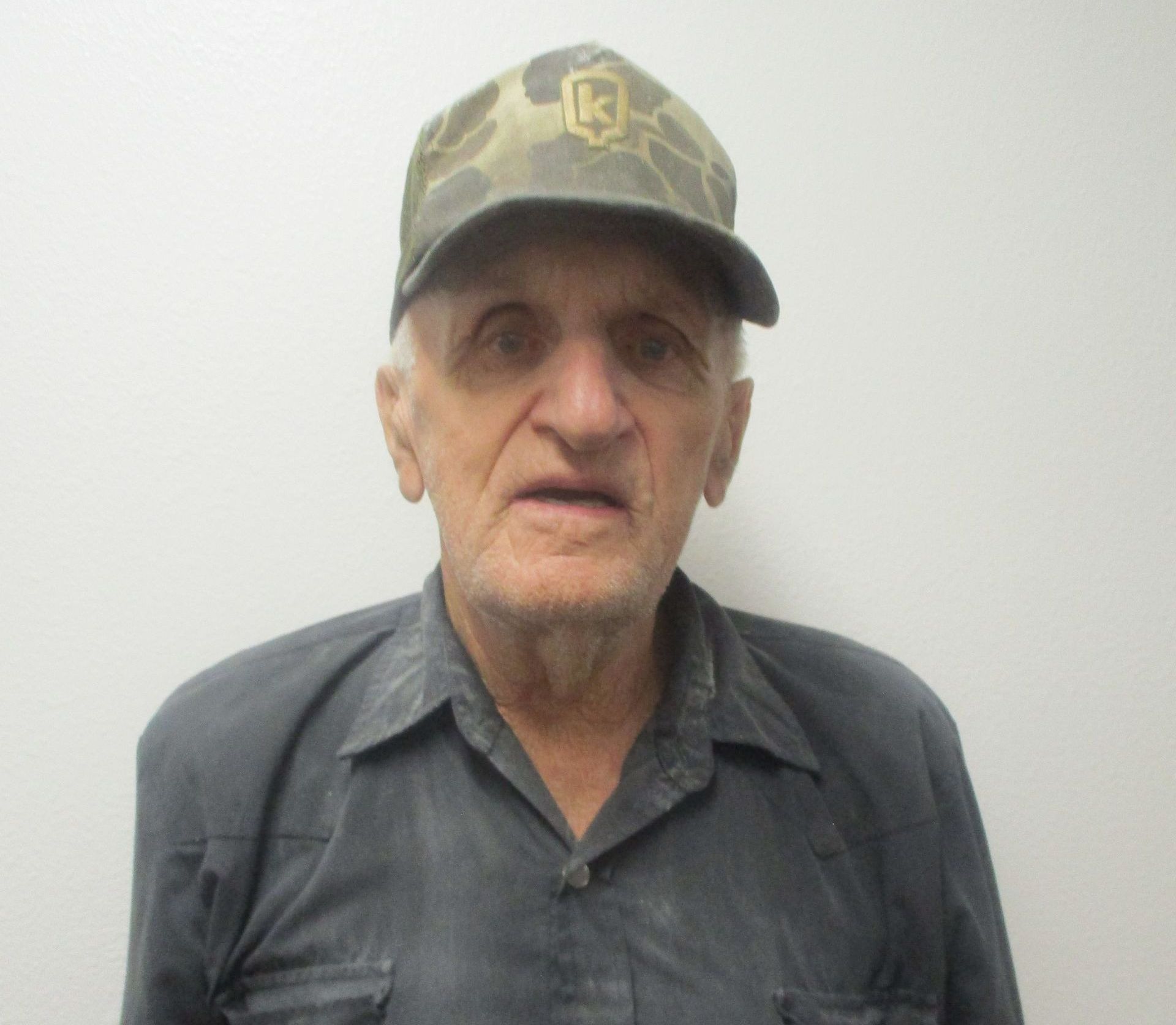 A man wearing a hat and a shirt is standing in front of a white wall.