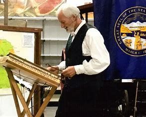 Man playing a musical instrument with a bow, in front of a state flag.
