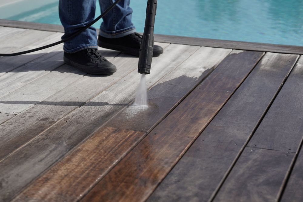 A person is cleaning a wooden deck with a high pressure washer.