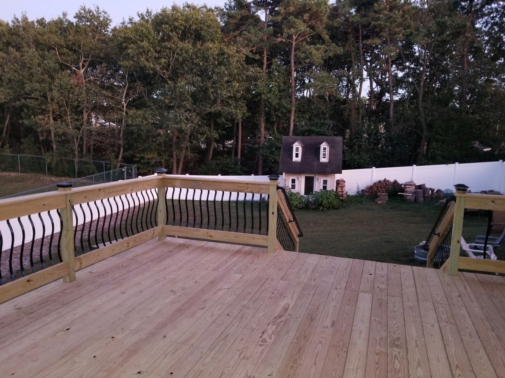 A wooden deck with a fence and a house in the background