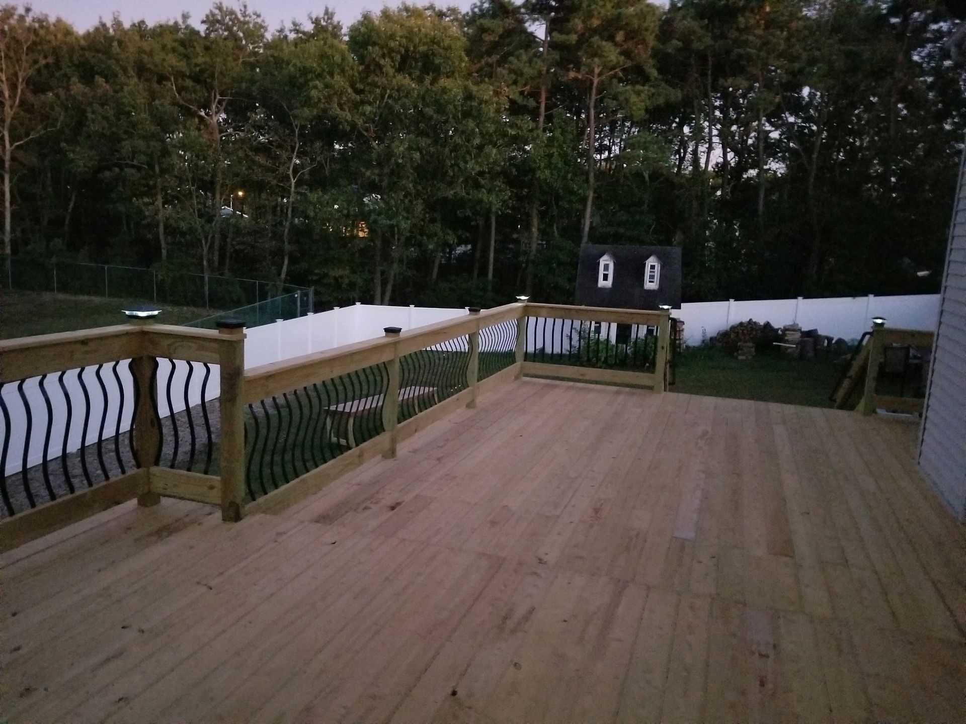 A wooden deck with a black railing and a fence in the background
