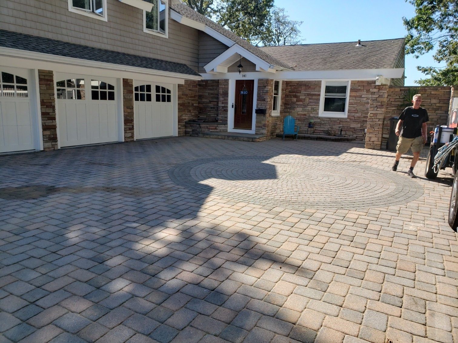 A man is standing in front of a house with a brick driveway.