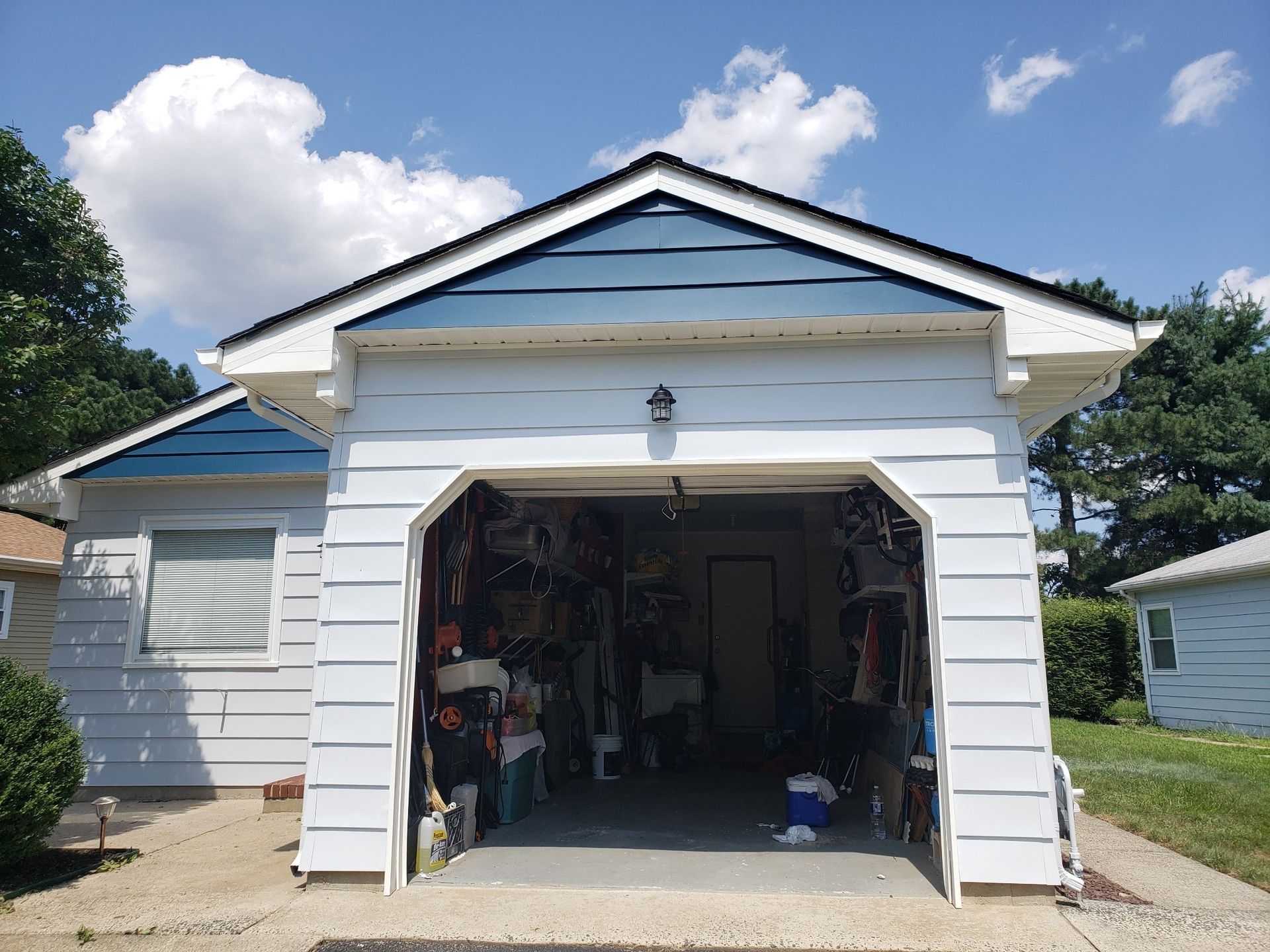 A white house with a blue roof and a garage with the door open.