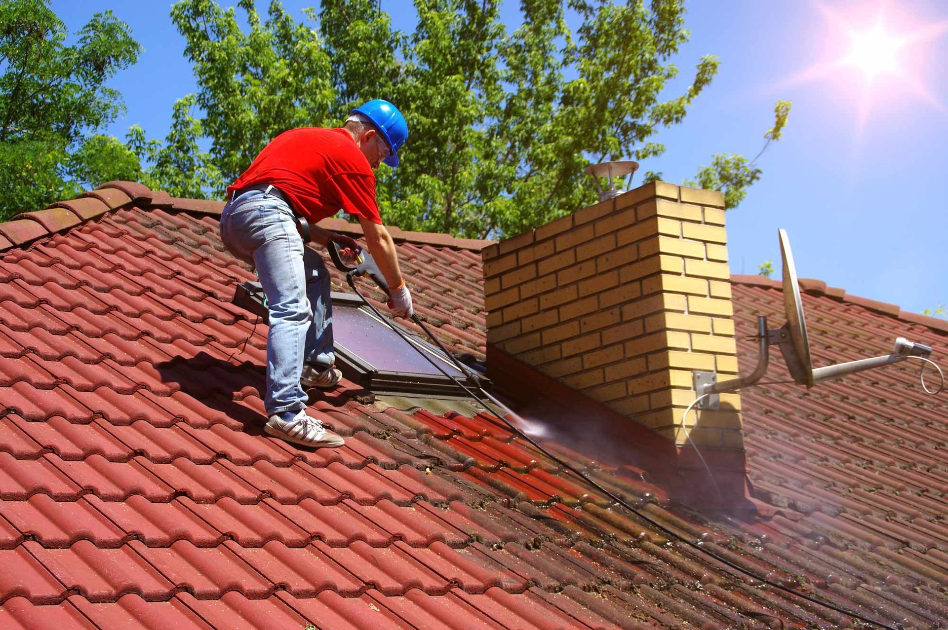 A man is cleaning the roof of a house with a high pressure washer.