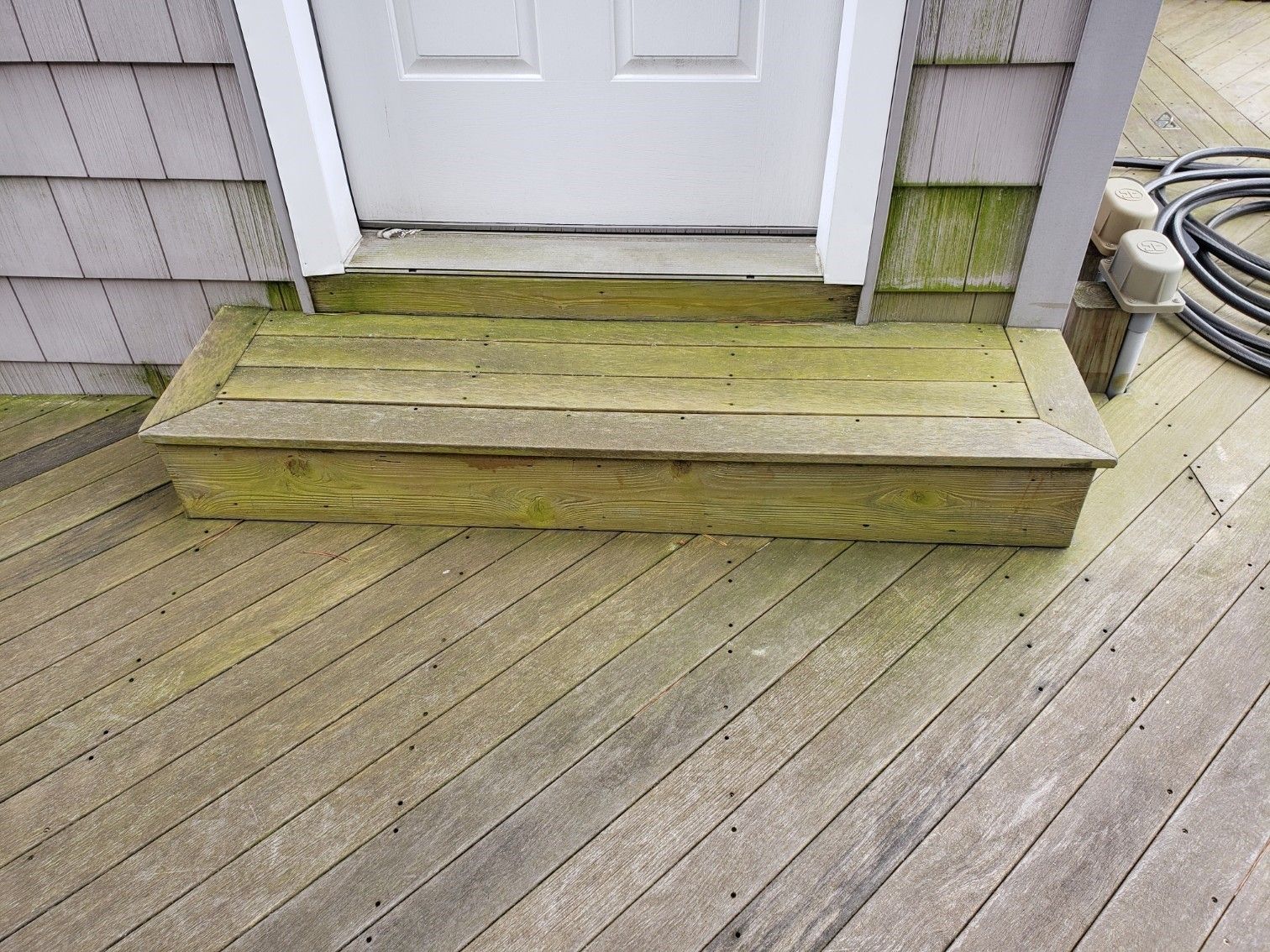 A wooden deck with steps leading to a white door.