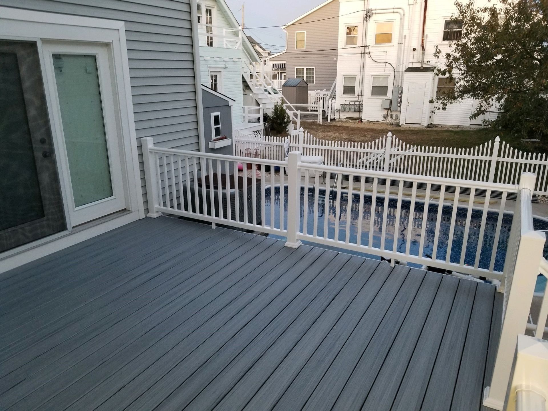 A gray deck with a white railing and a pool in the background.
