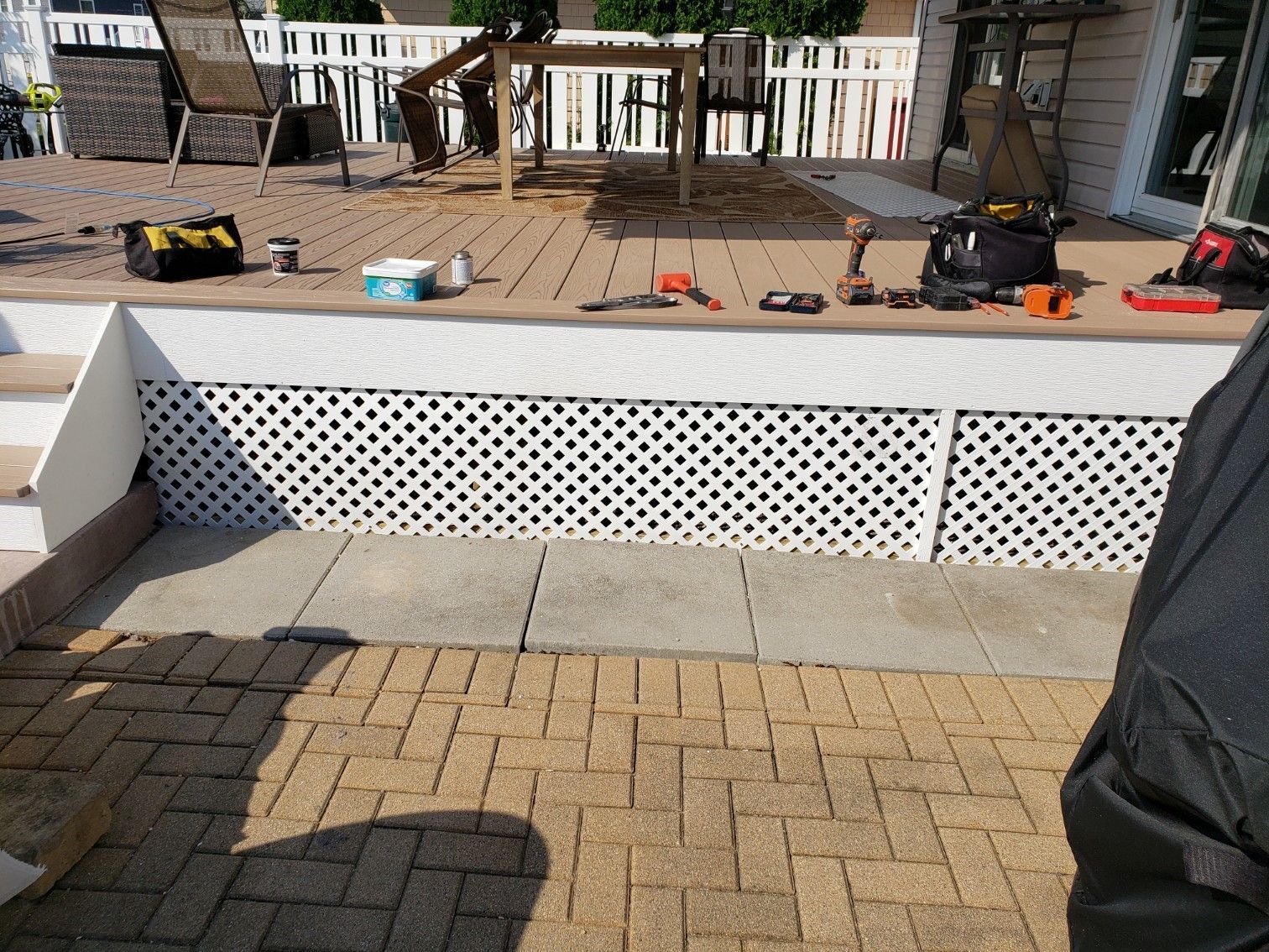 A person is standing on a brick patio next to a deck.