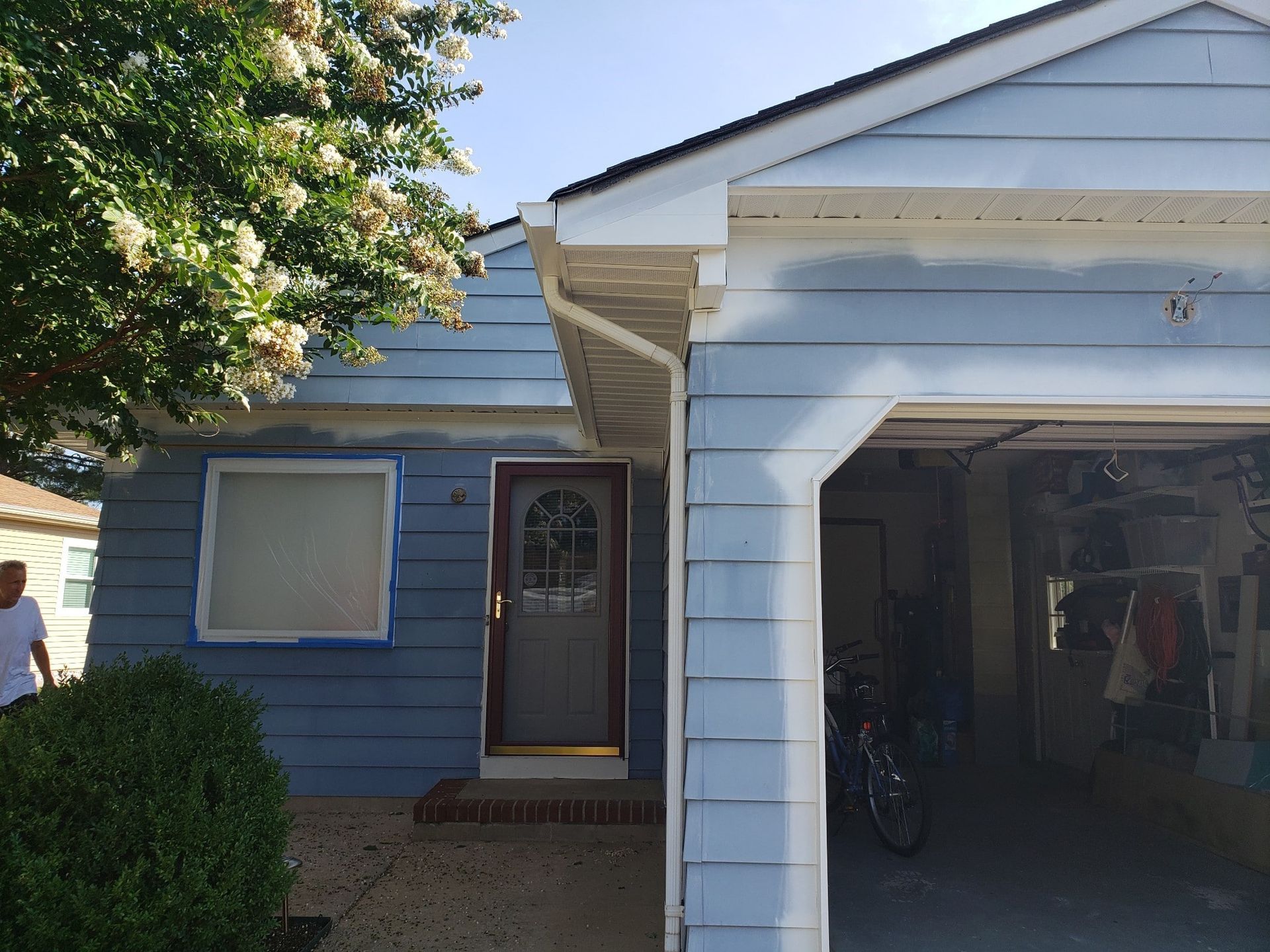 A man is standing in front of a blue house with a garage.