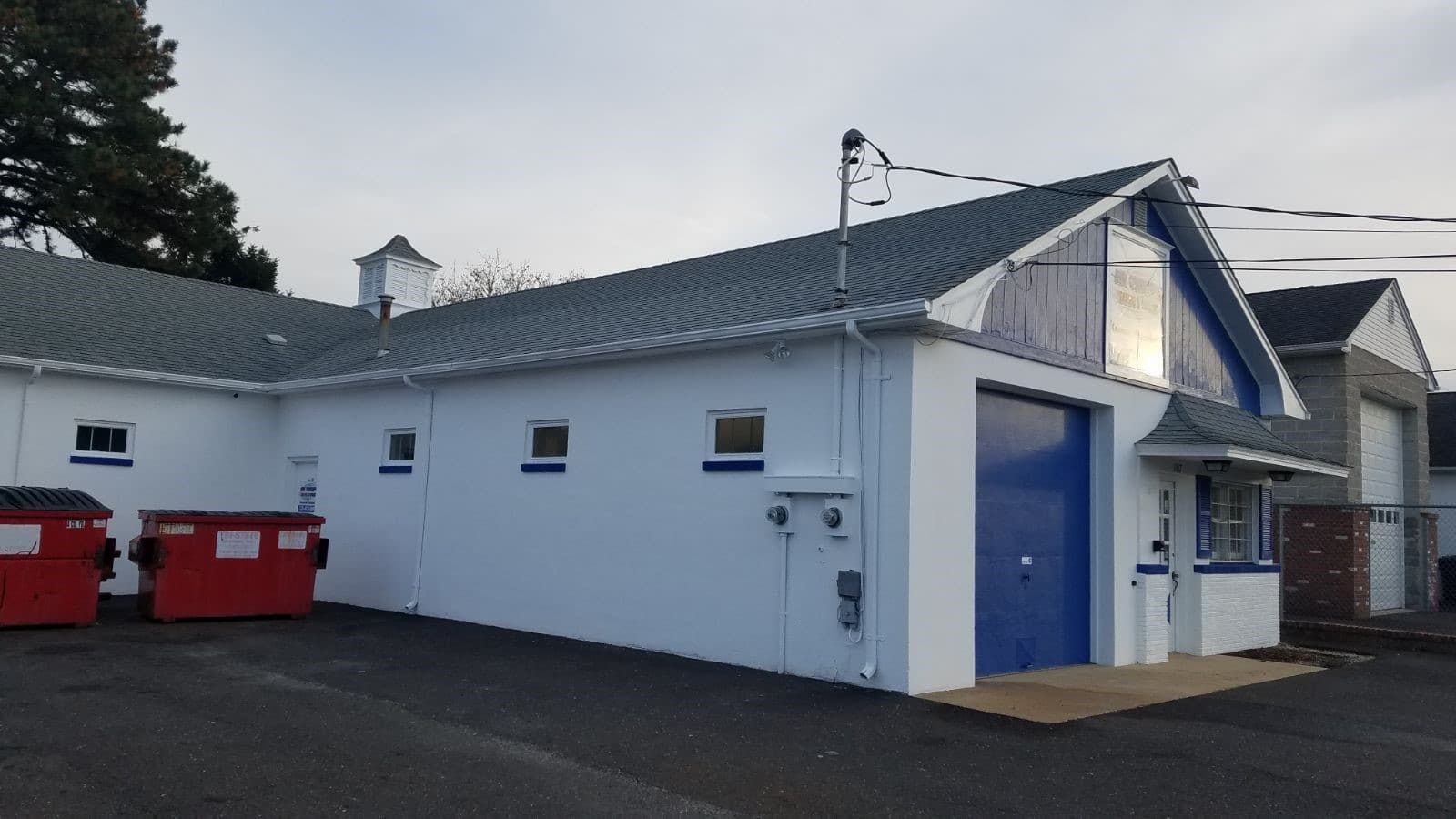 A white building with a blue door and a red dumpster in front of it