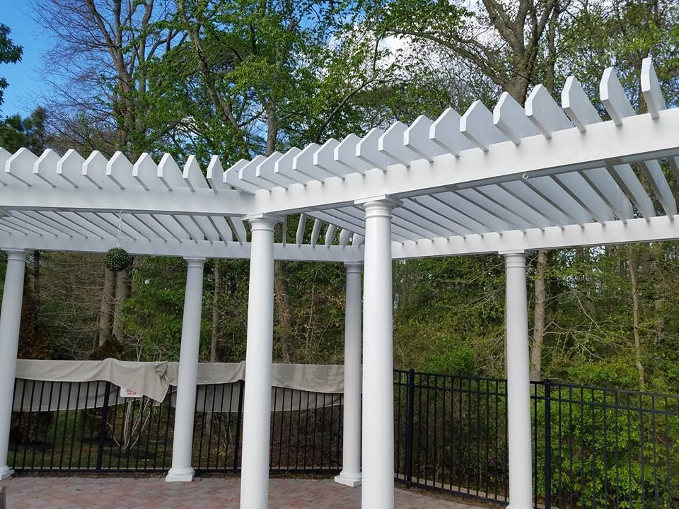 A white pergola with a black fence and trees in the background