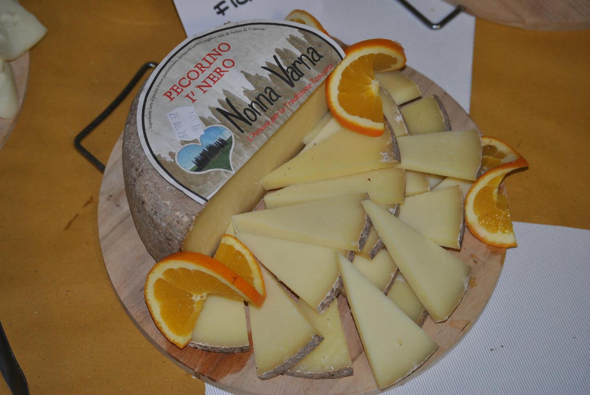 Piatto di formaggi con formaggio a fette, spicchi d'arancia e una forma di formaggio rotonda.