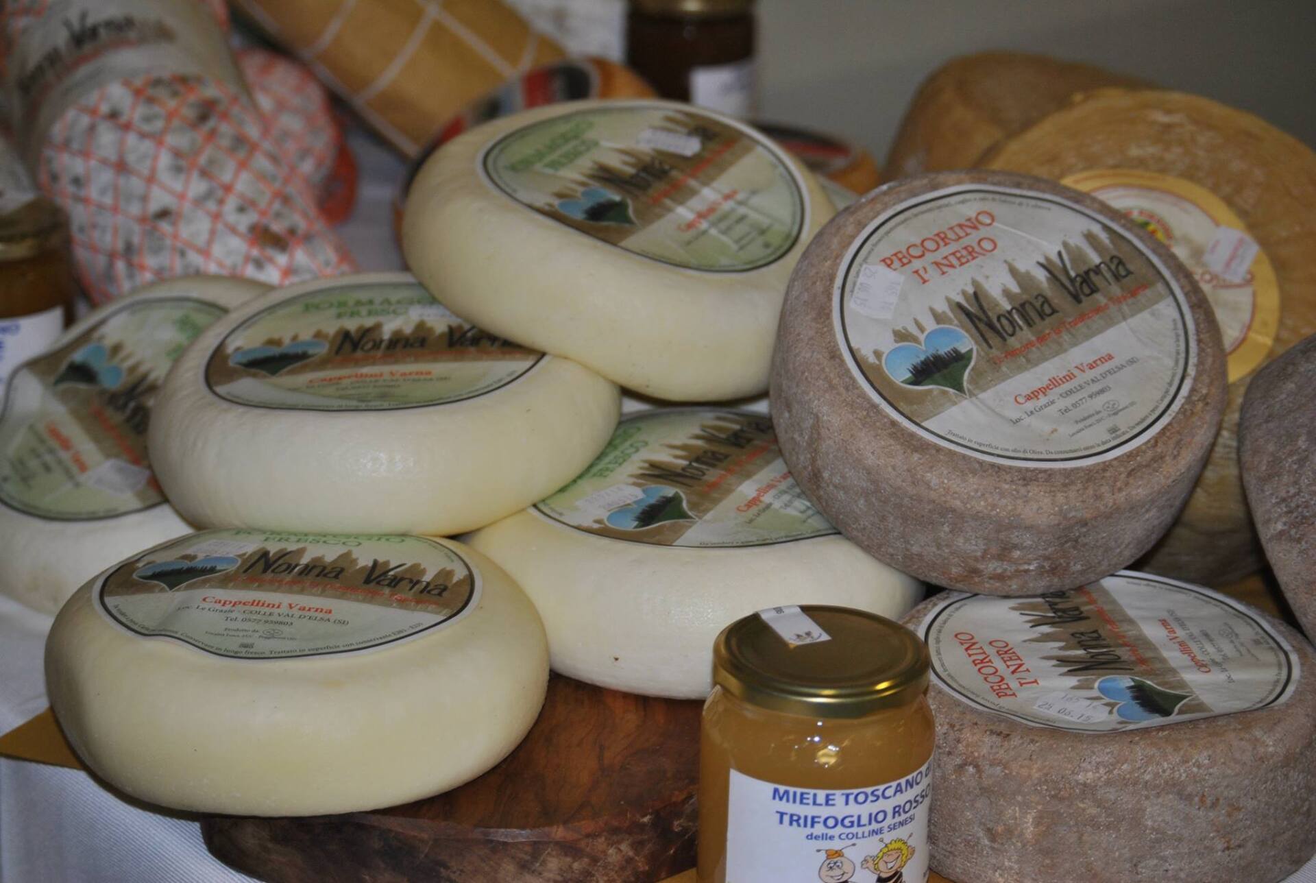 Esposizione di vari formaggi, alcuni con etichette, e un barattolo di conserve.
