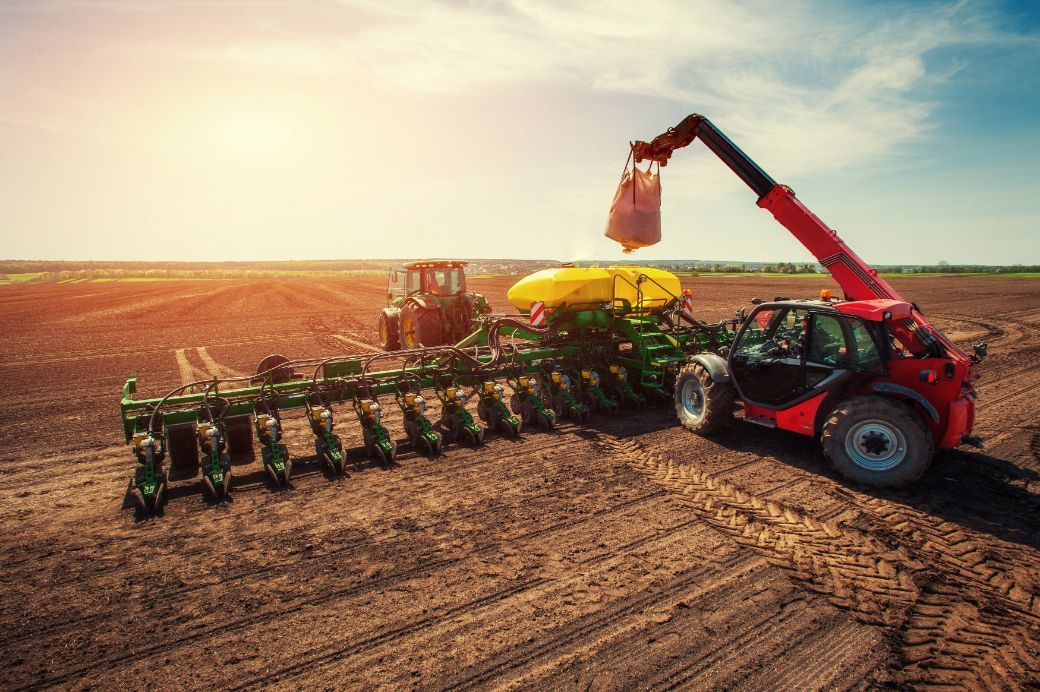 A tractor is plowing a field with a crane attached to it. Services Tall Crop 620-617-1662