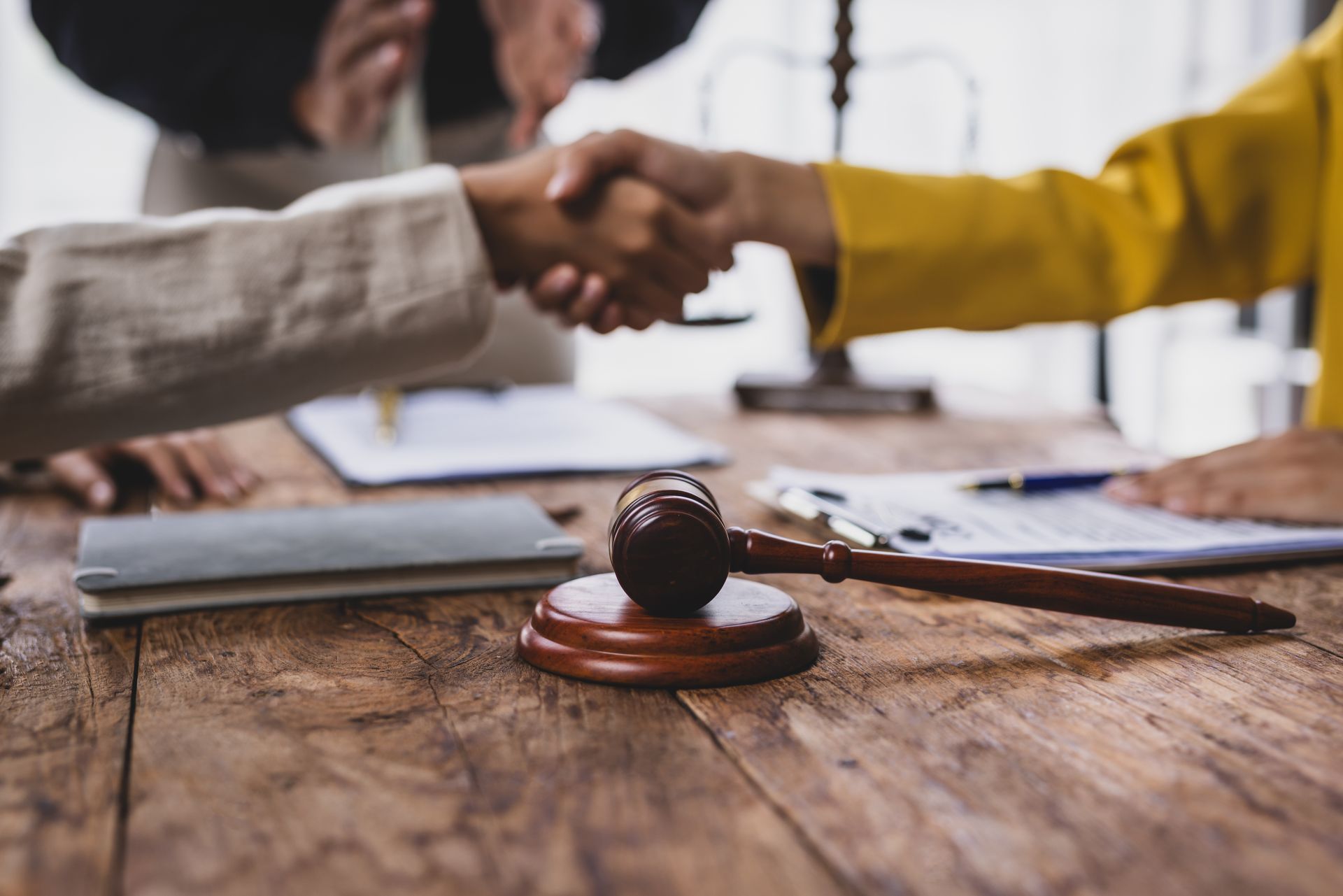 A legal gavel on a desk with clients shaking hands after a meeting with employment law attorneys.