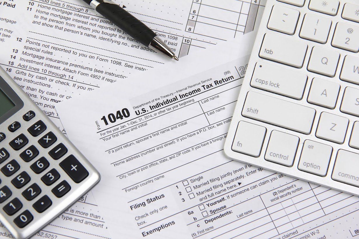 Tax documents, calculator, pen, and keyboard on a desk.