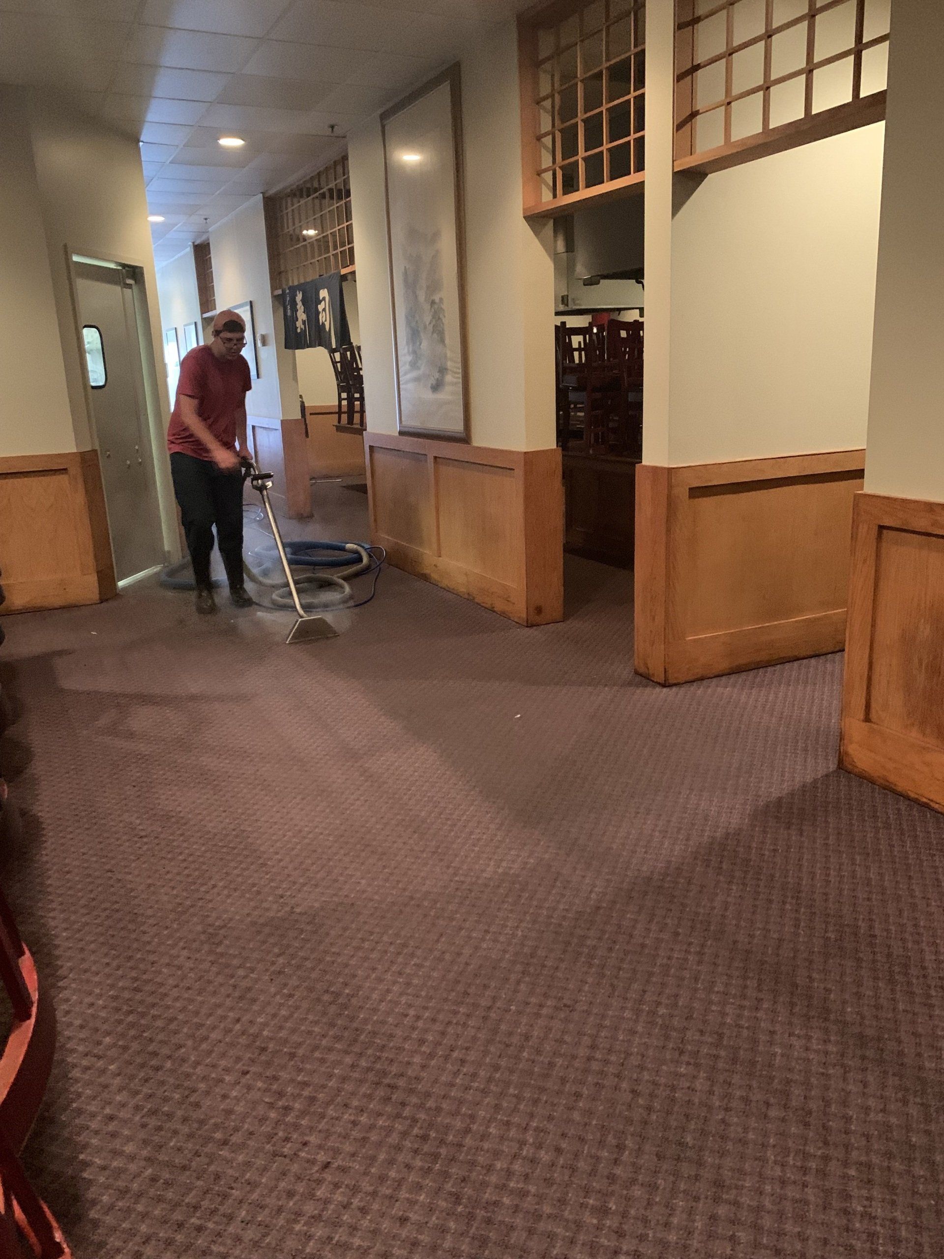 A man is cleaning a carpet in a hallway with a vacuum cleaner.
