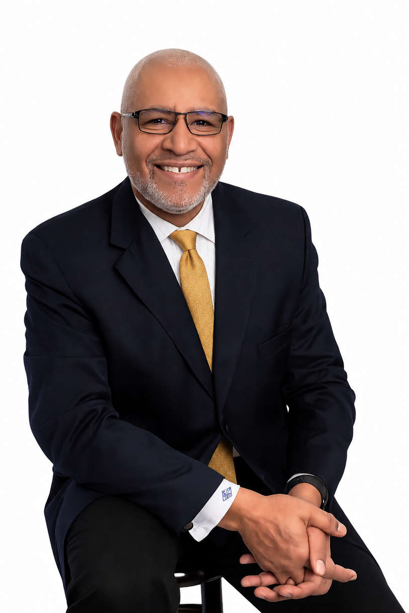 Smiling man in a dark suit with a gold tie, seated against a white background.