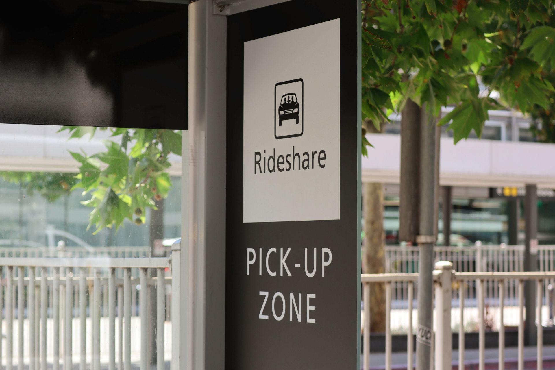 Rideshare pick-up zone sign beside a covered curbside area and trees