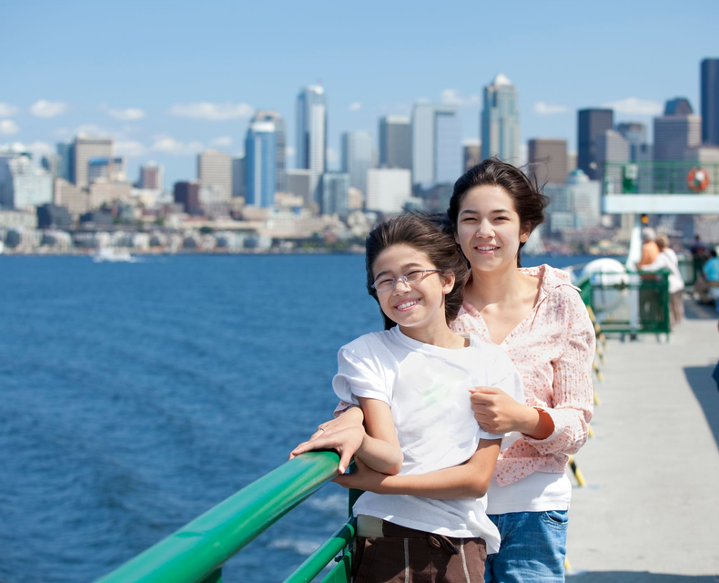Two people smiling on a waterfront promenade with the Seattle skyline in the background