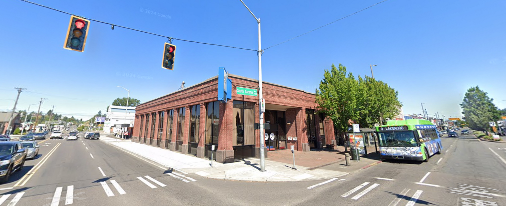 Street intersection with a brick corner building, red traffic lights, and a bus stopped on the right.