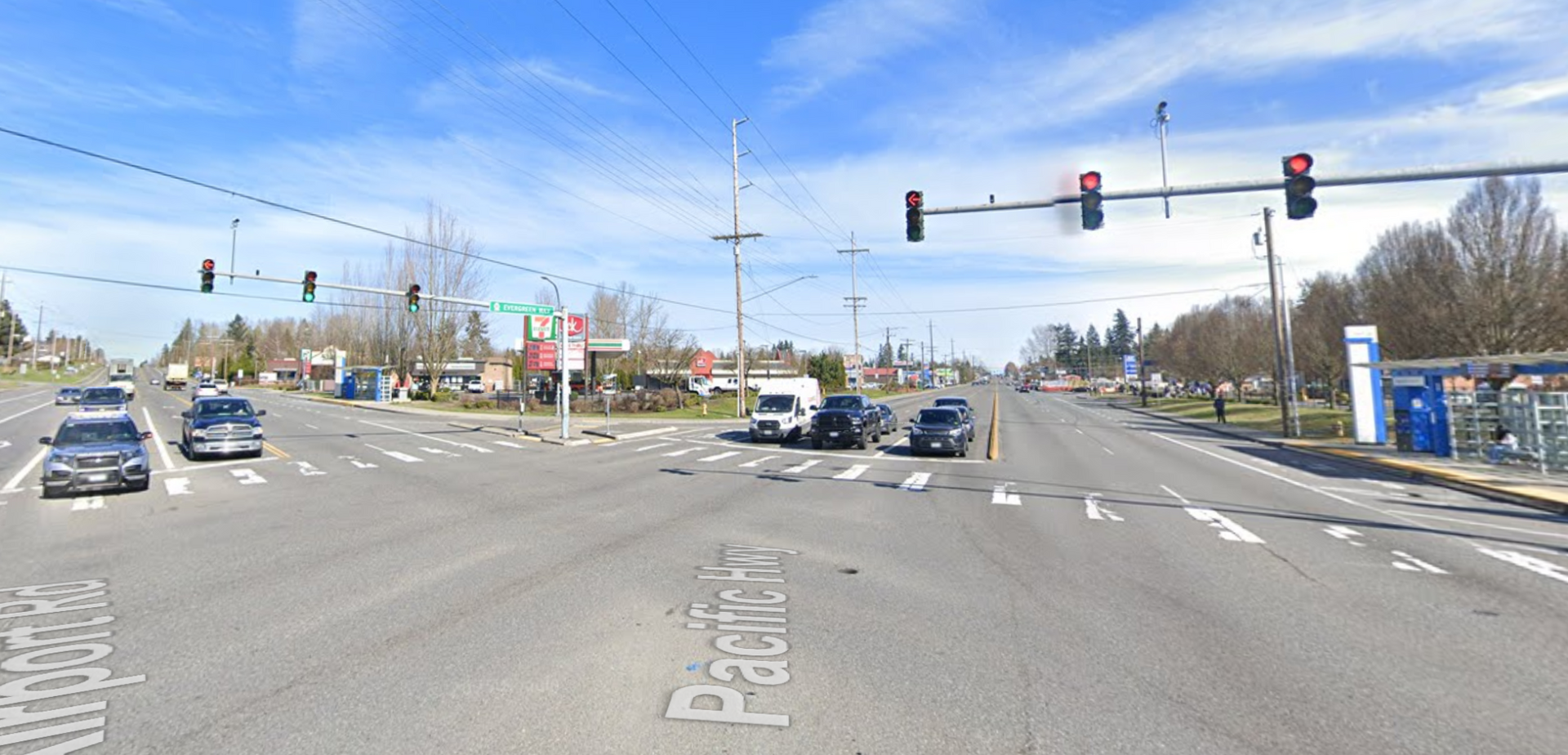 Wide intersection with multiple cars stopped at red traffic lights on a clear day.