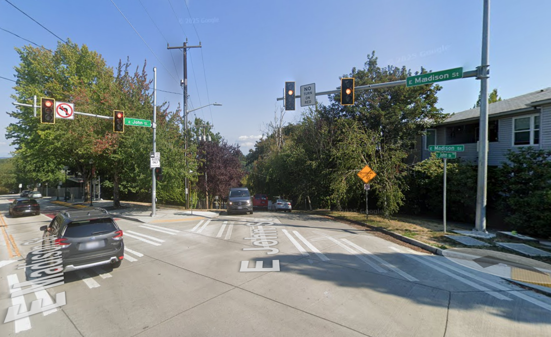 Urban street intersection with traffic lights, crosswalks, cars, and trees on a sunny day