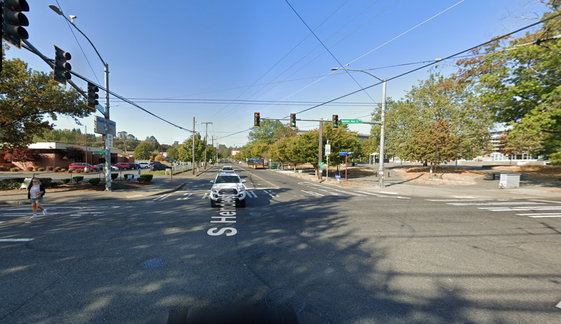 Wide city intersection with a few cars, trees, and overhead wires on a clear day