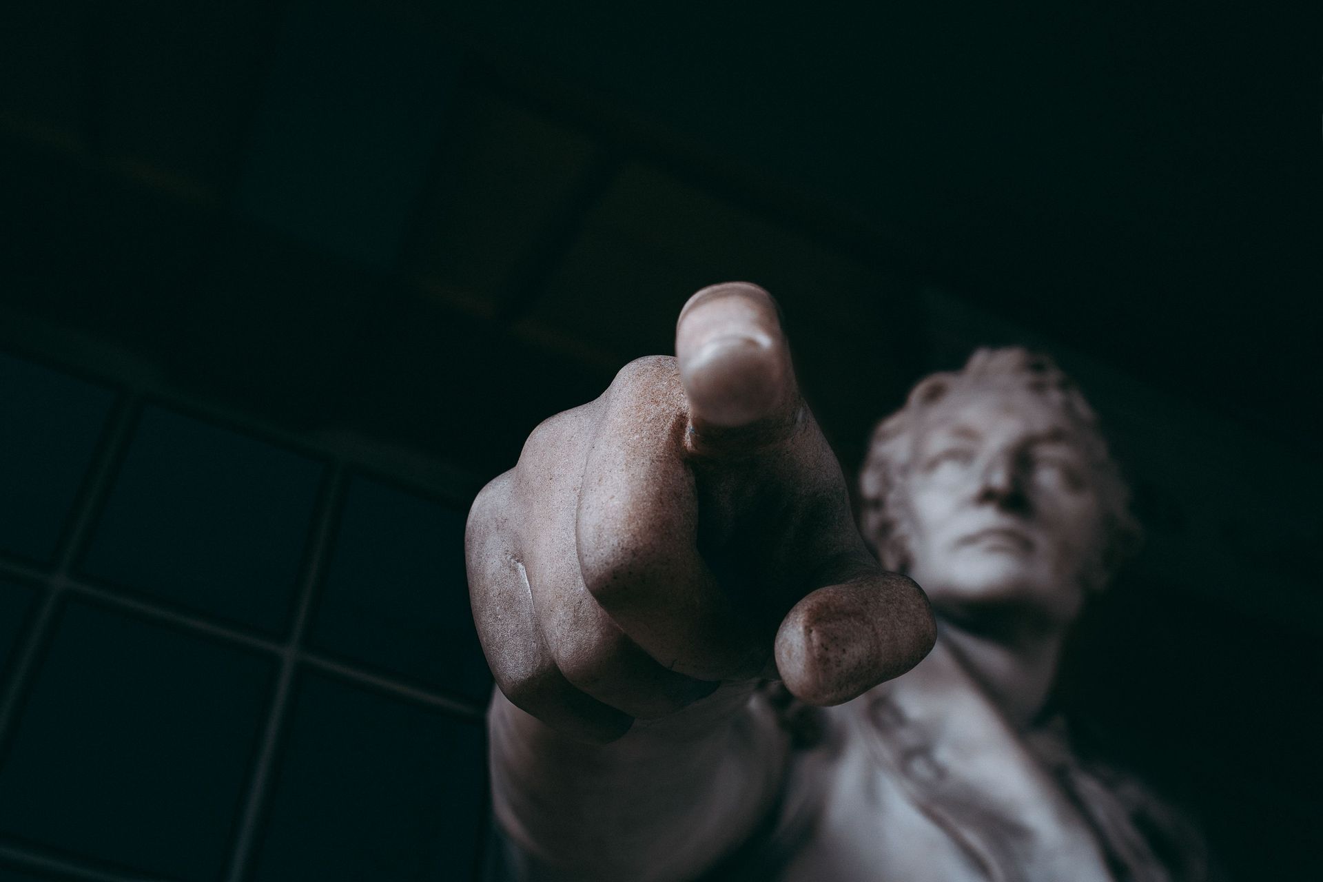 Statue-like figure pointing at the viewer in a dark, green-tinted setting