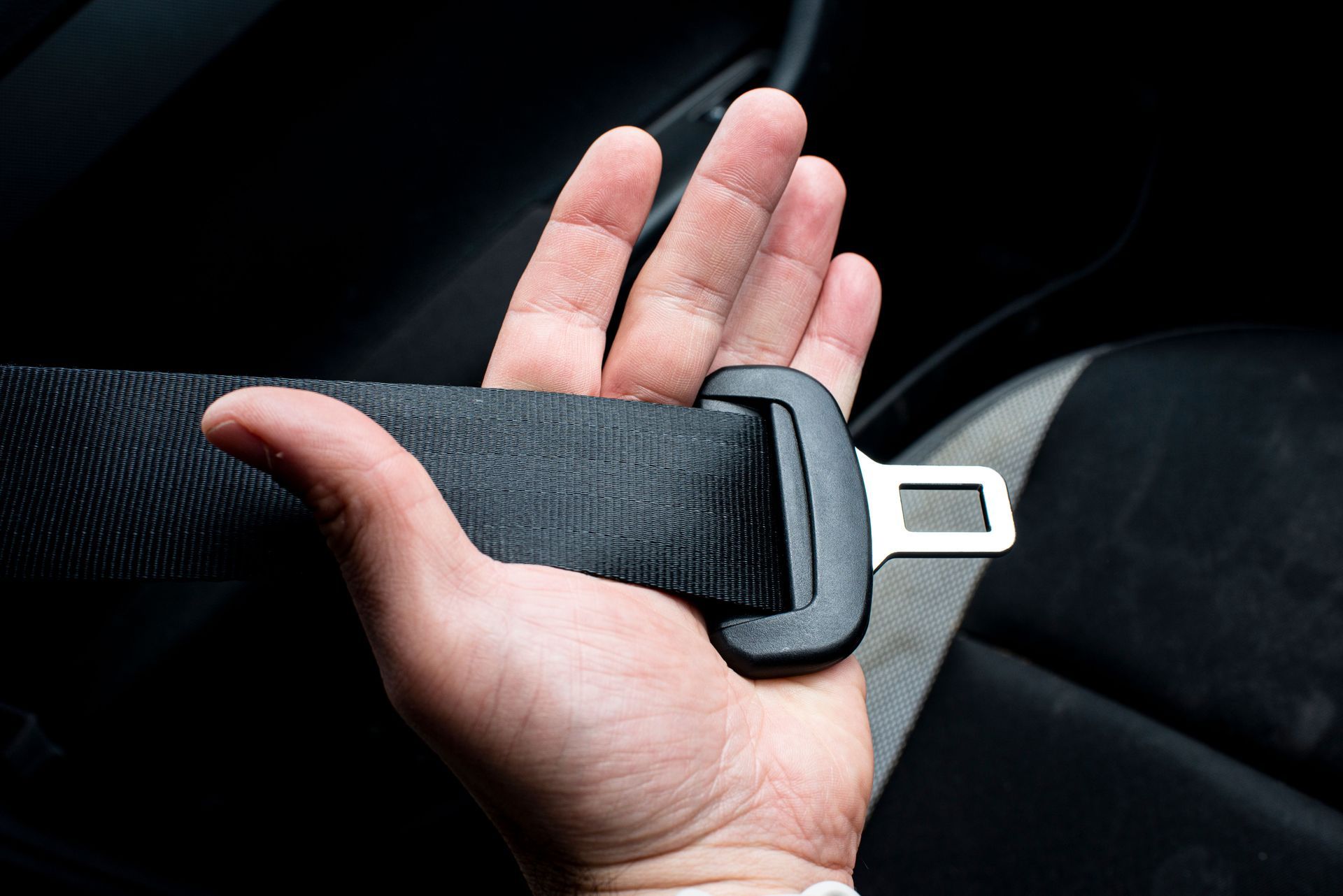 Hand holding a black seat belt buckle and strap inside a car