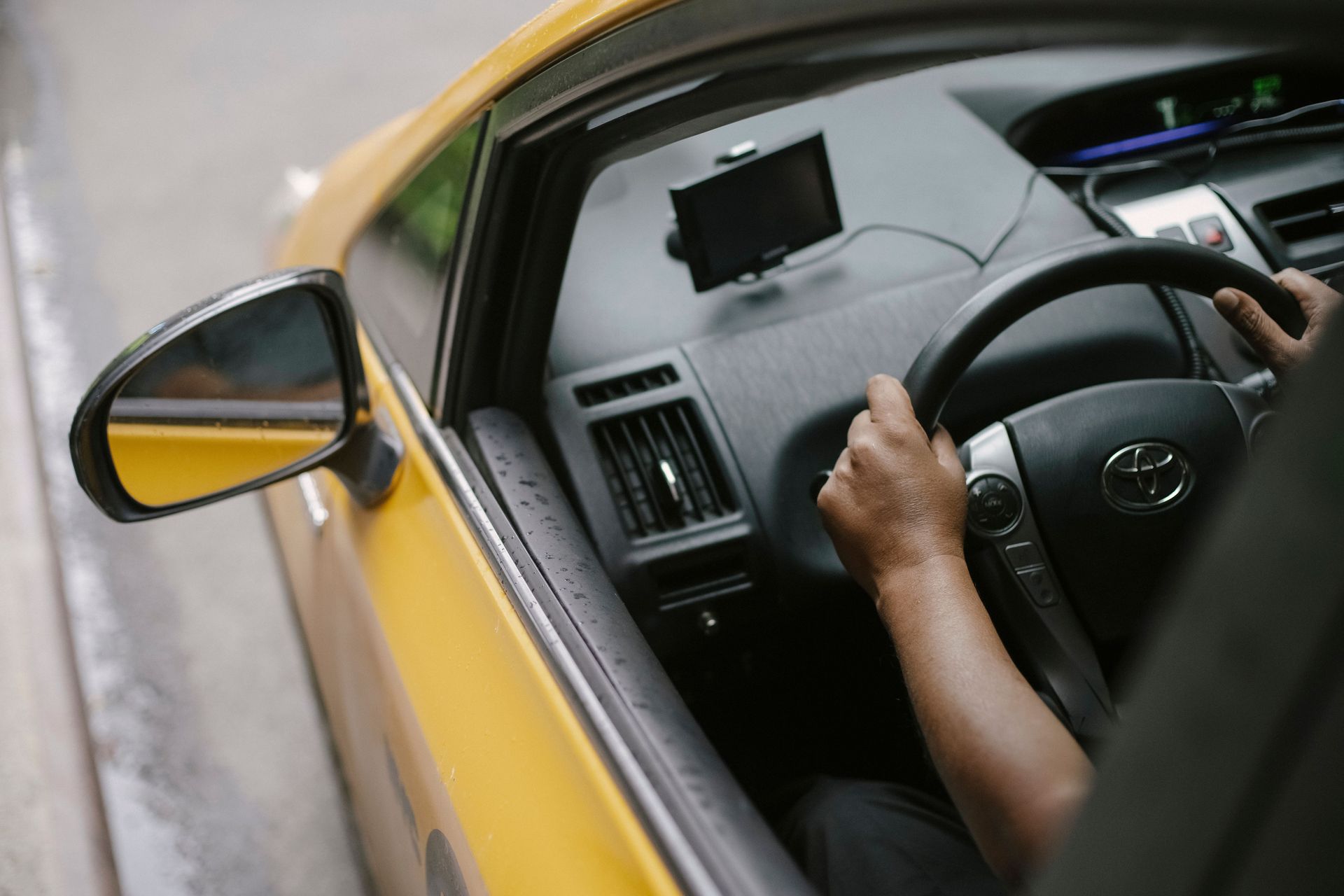 Driver’s hands on the wheel inside a yellow car on a city street