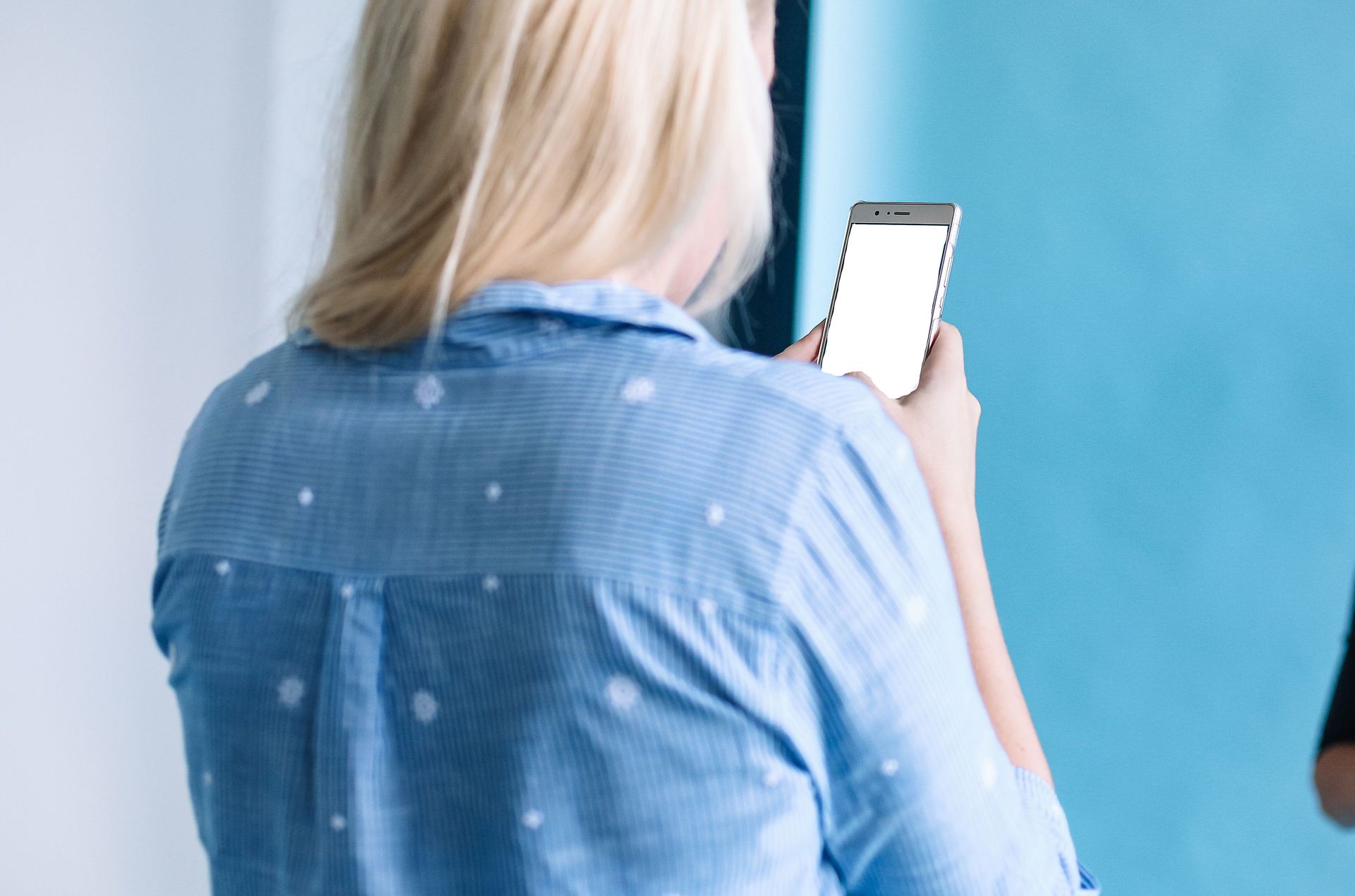 Person in a blue shirt holding a smartphone and taking a photo against a blue wall