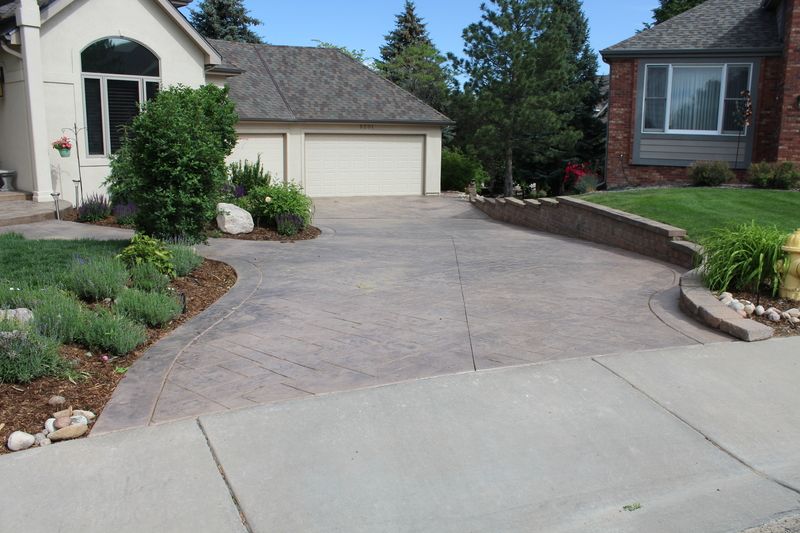 Driveway leading to a house with landscaping. The driveway is gray, house is beige.