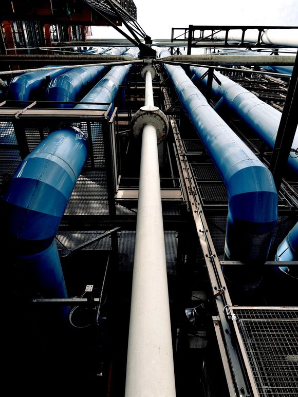 Industrial pipes and ducts in blue and white, viewed from below in a metal factory setting