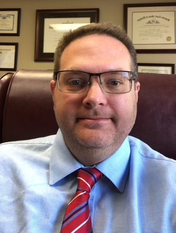 Man in glasses and tie, in an office, facing the camera.