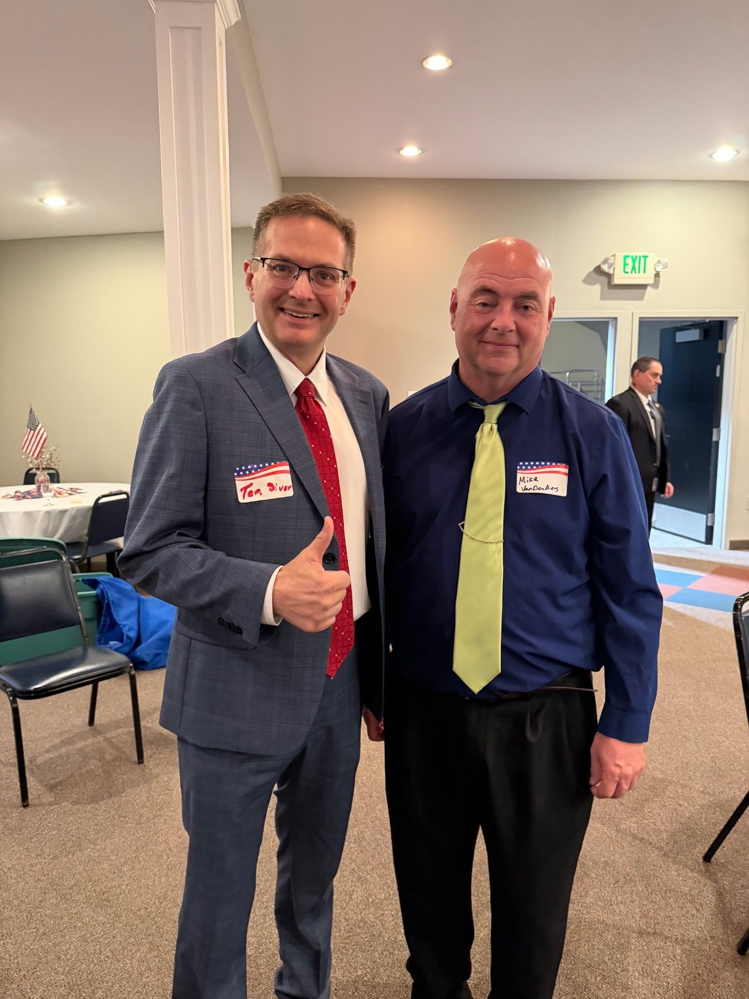 Two men in business attire smiling and posing indoors at an event