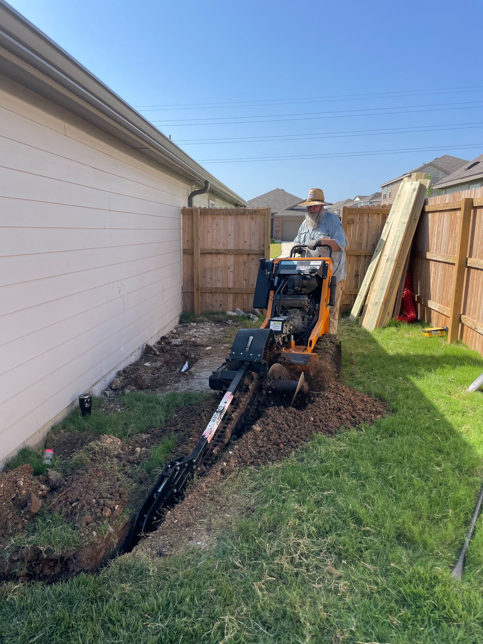 A man is driving a small excavator in a backyard.