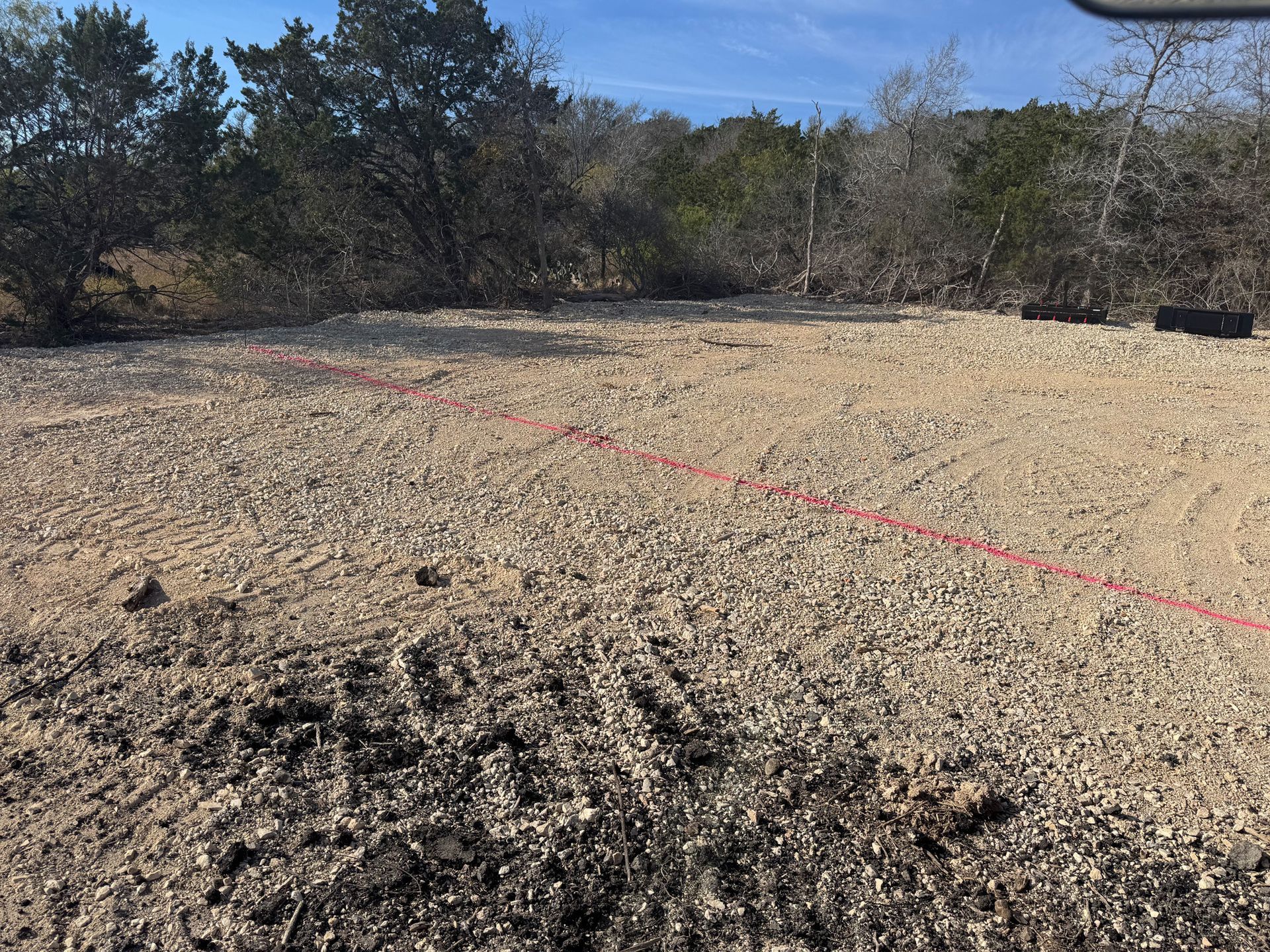 A dirt field with trees in the background and a red line on the ground.