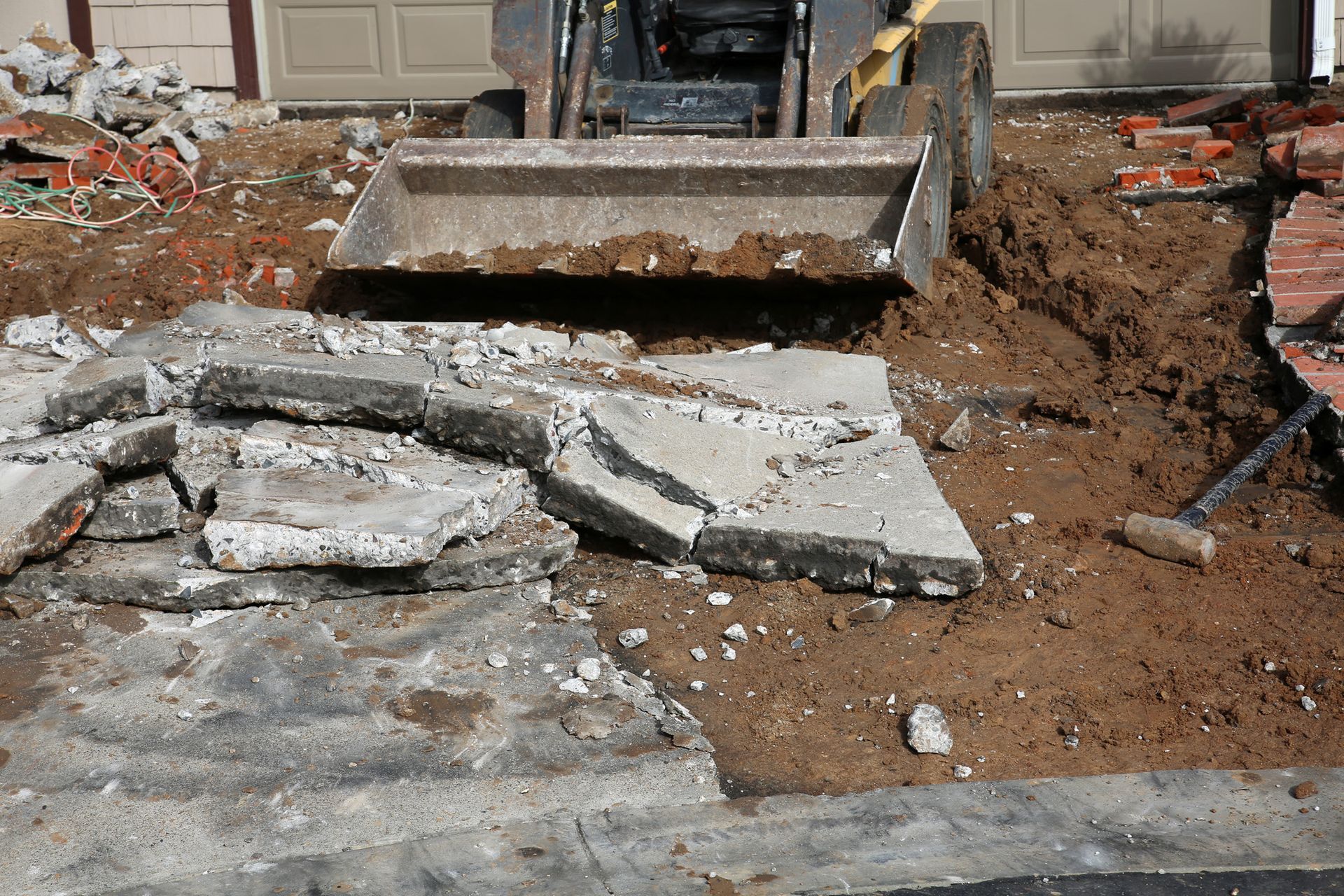 A bulldozer is demolishing a concrete driveway in front of a garage