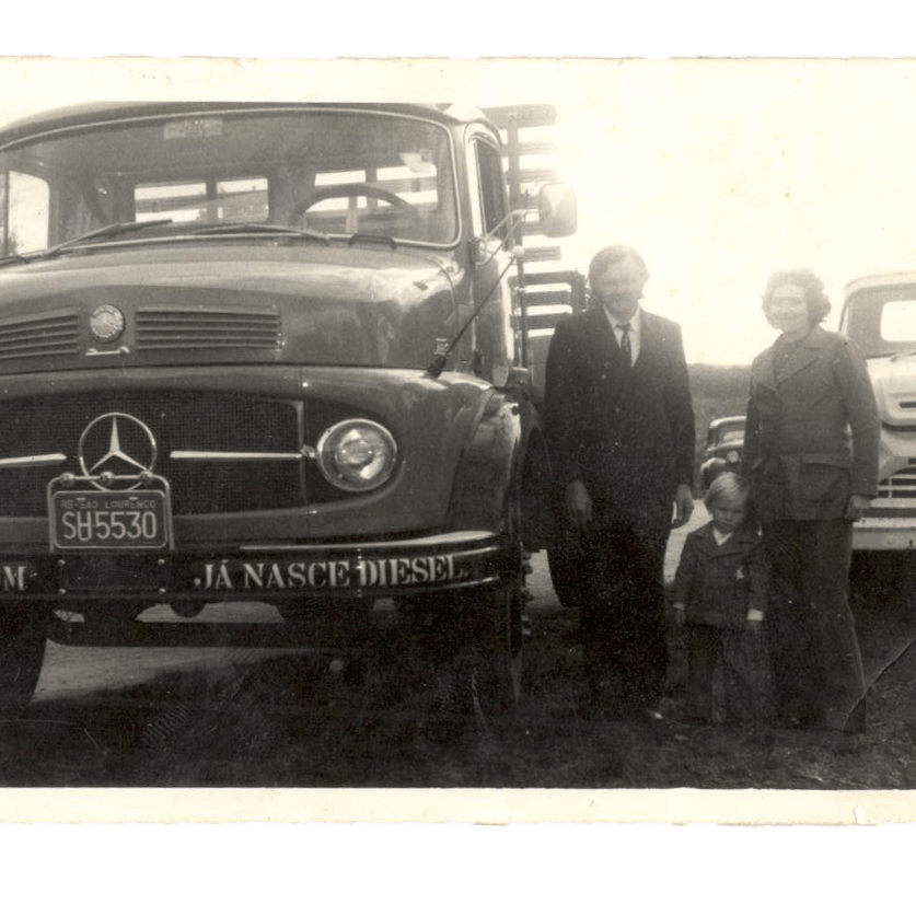 Uma caminhonete Mercedes-Benz antiga estacionada ao ar livre ao lado de três pessoas que estão em pé juntas.