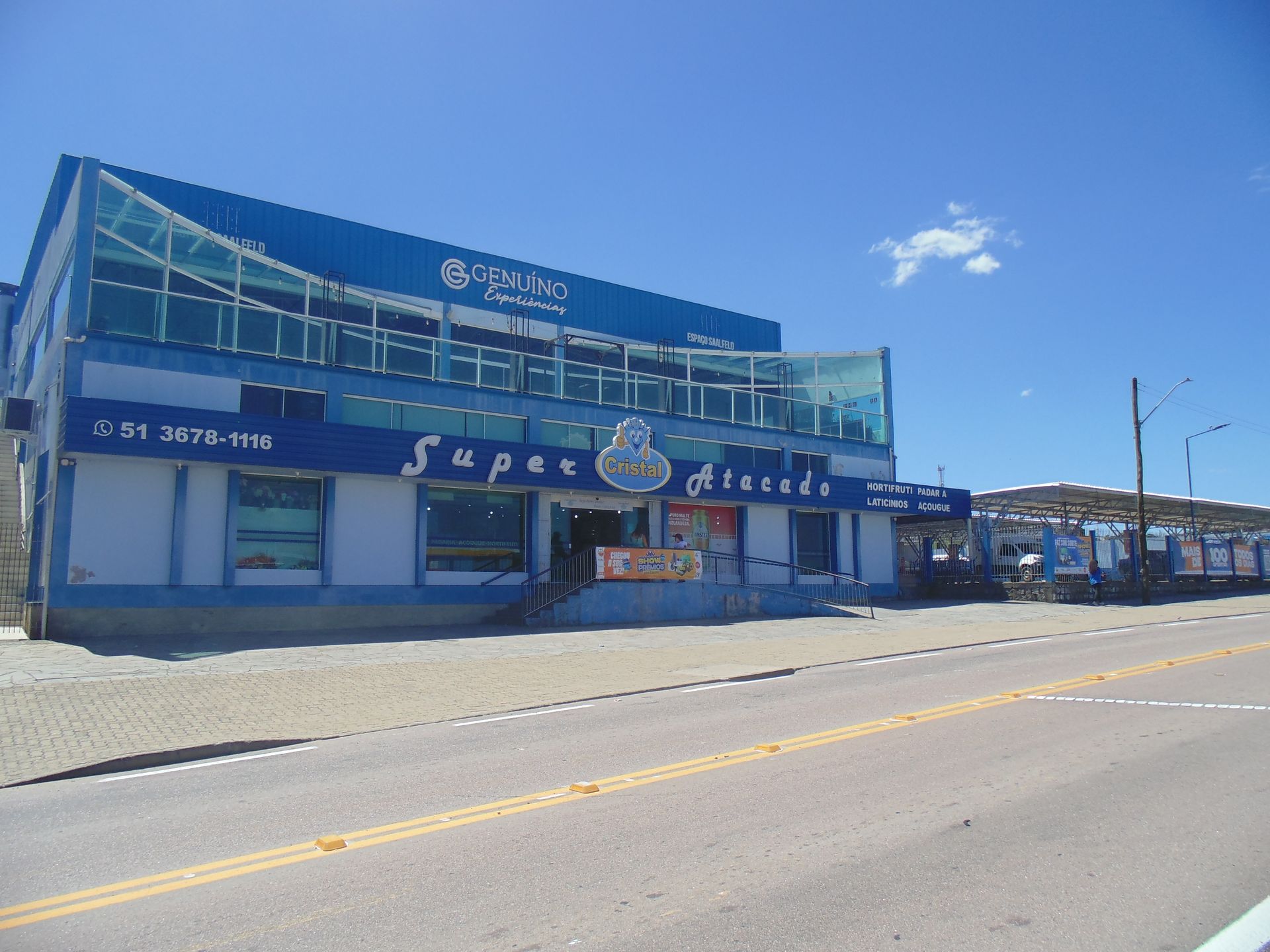 Um supermercado Super Atacado de dois andares, azul e branco, visto da estrada em um dia ensolarado.