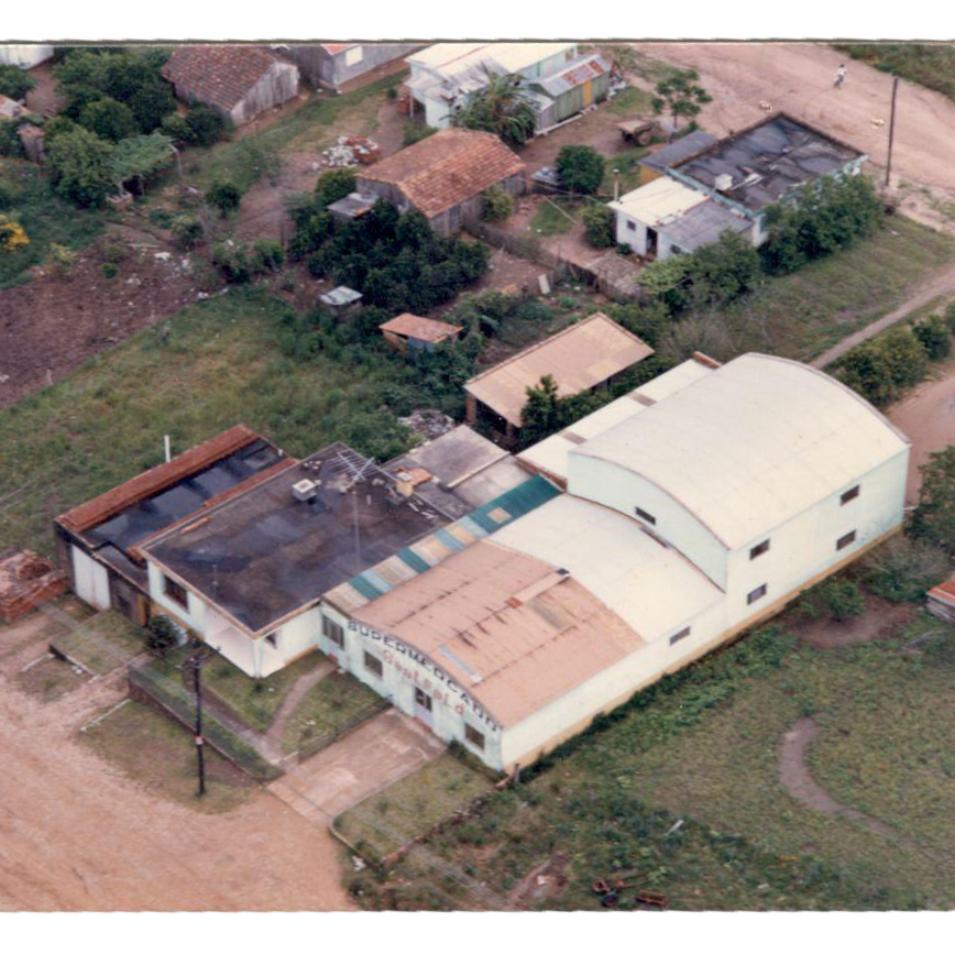 Vista aérea de um complexo de edifícios comerciais de cor clara, situado entre casas e espaços verdes.