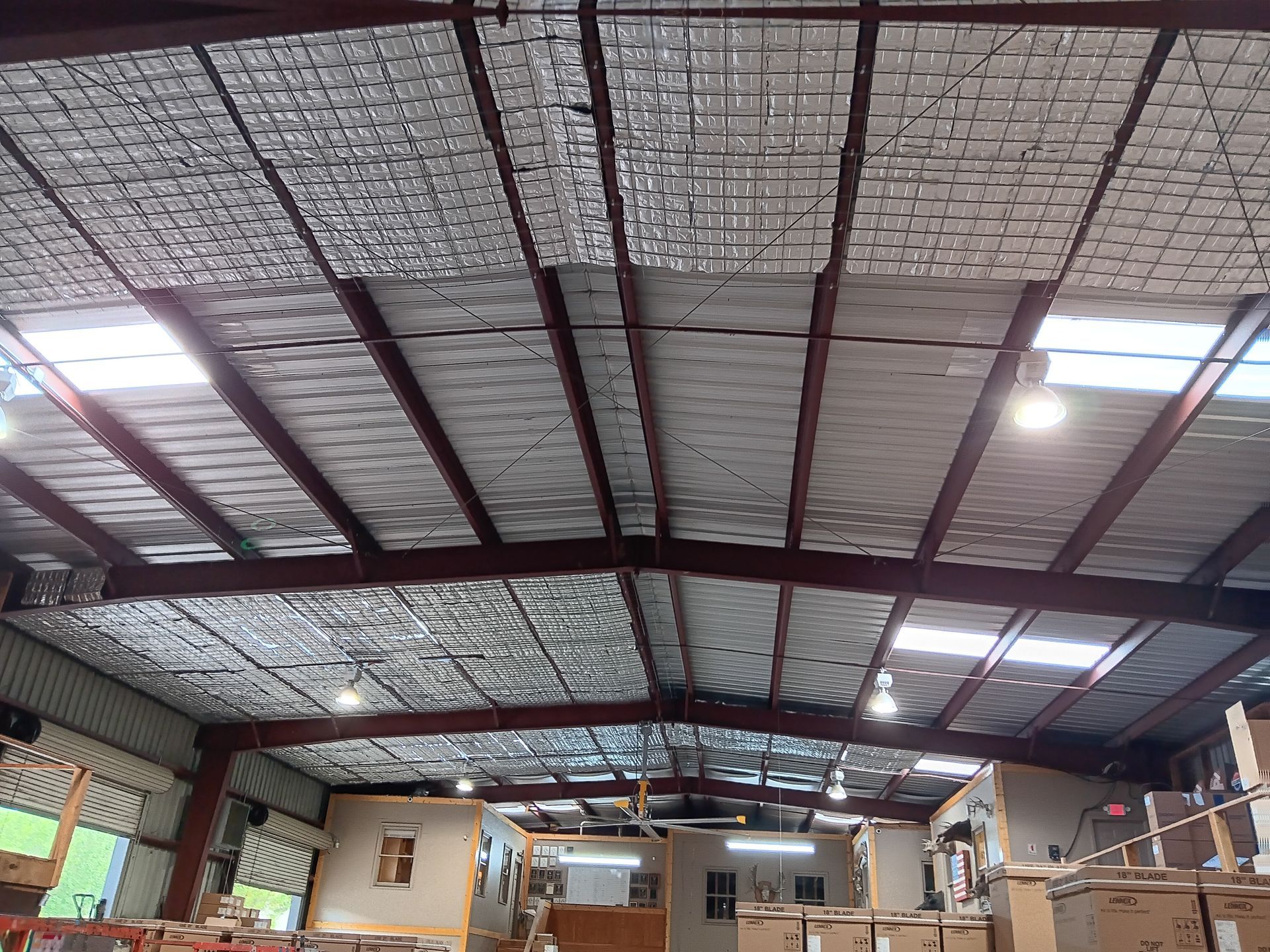 Warehouse interior with red steel beams supporting a silver insulated roof and skylights.