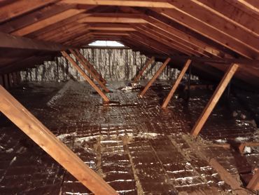 Interior of an attic with wooden beams and insulation visible.