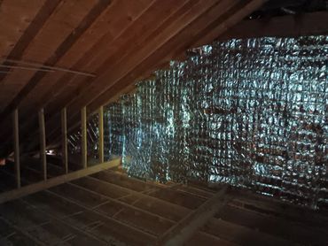 Attic interior with silver reflective insulation installed between wooden rafters.