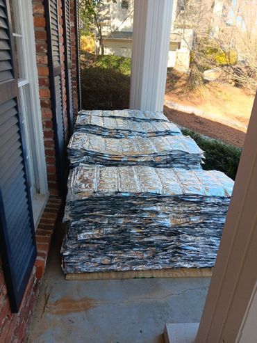 Stacks of silver insulation material on a porch next to a brick wall and window.