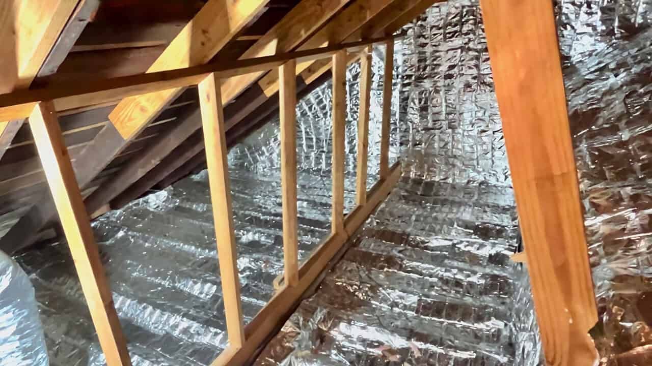 Wooden attic framing with silver radiant barrier insulation.