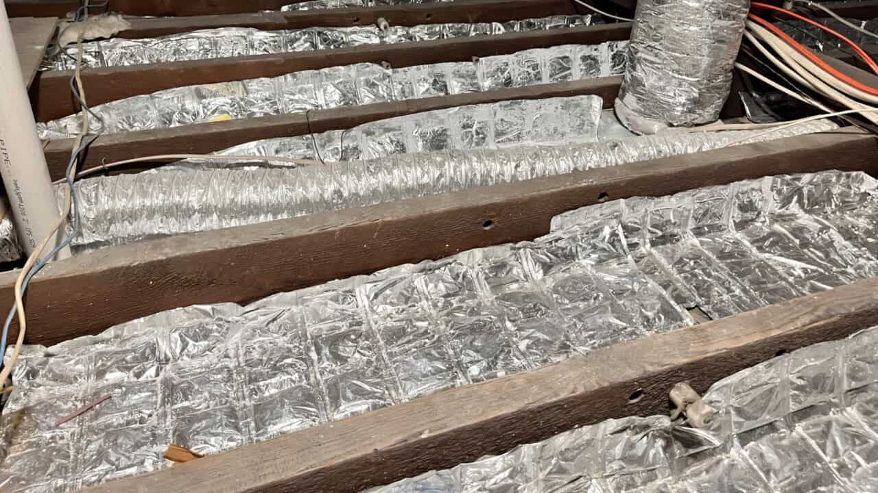 Attic insulation between wooden beams, with ductwork and wiring visible.