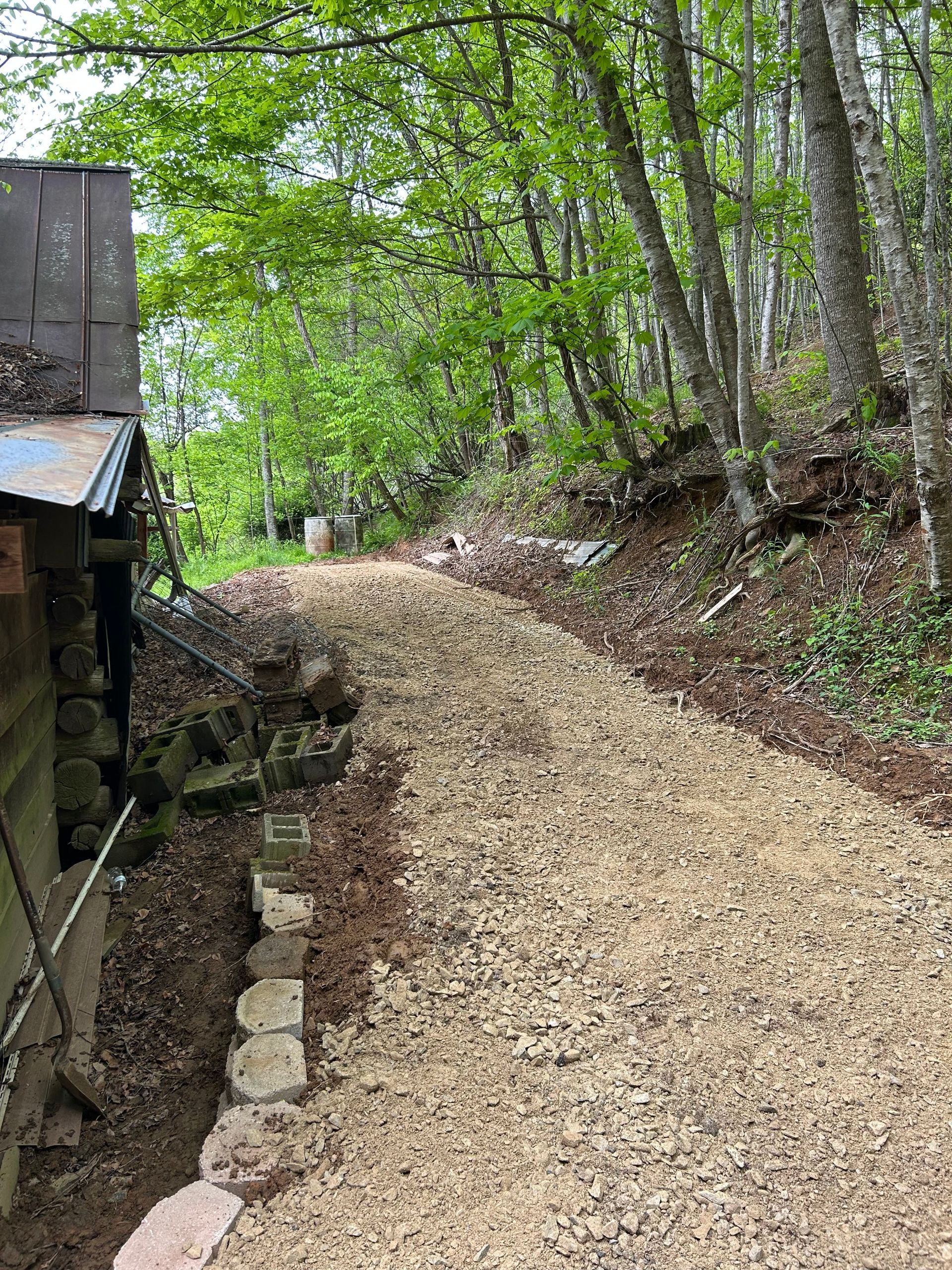 Gravel path curving uphill through a wooded area beside a rustic cabin and stacked stones