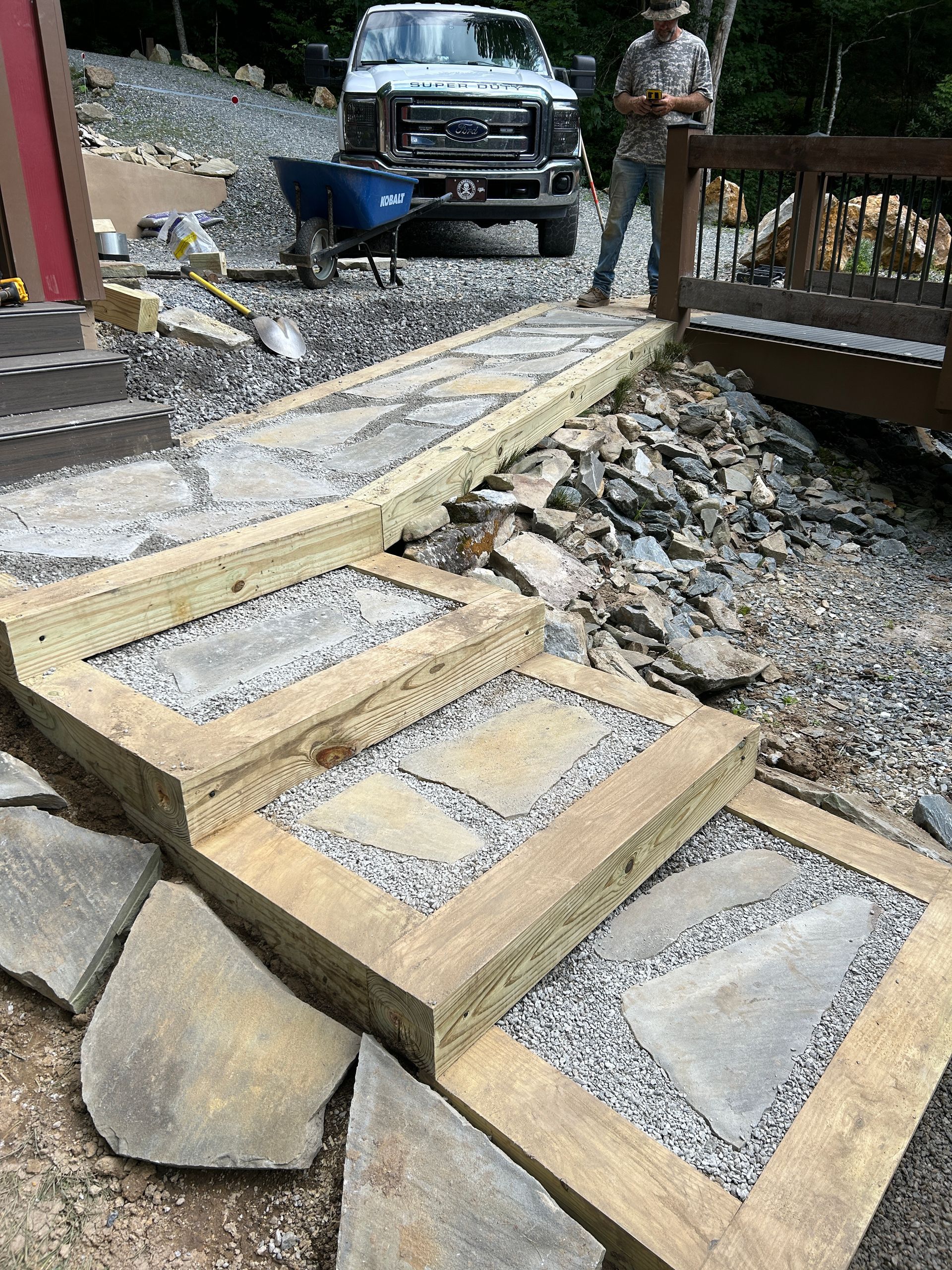 Stone steps on a rocky slope leading to a walkway, with a truck and a person in the background.