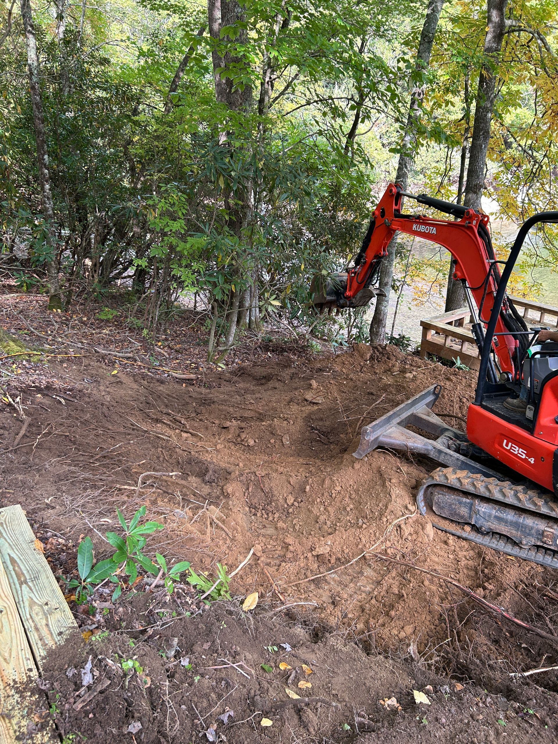 Red excavator clearing dirt on a wooded hillside trail.